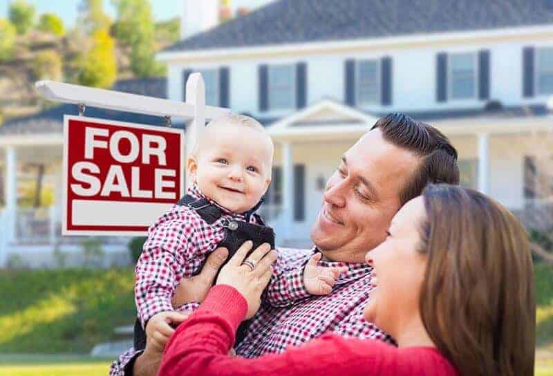 A couple holding their baby in front of a house for sale