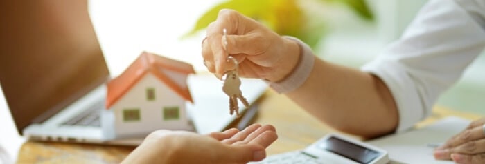 close up of two peoples hands, one person is handing the keys to a house to another person