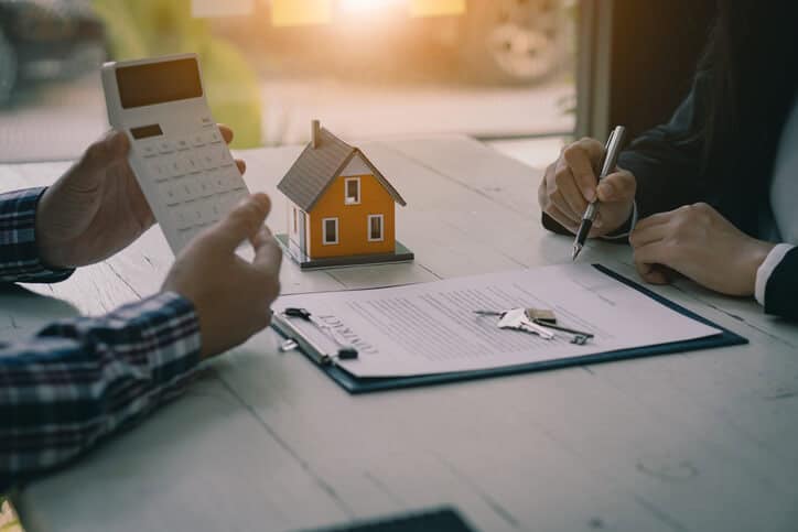 A man in a plaid shirt showing a calculator to another man filling out real estate paperwork