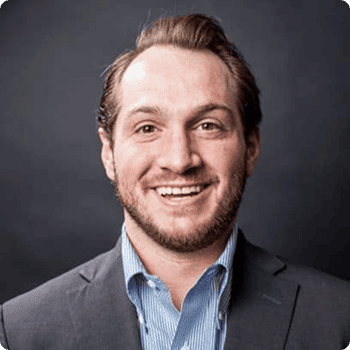 Professional headshot of a smiling man wearing a dark blazer and light blue shirt.